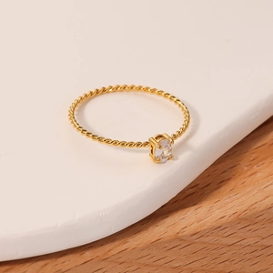 Elegant gold twisted rope ring with round zircon on white stone surface with wood texture