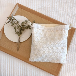 Detailed close-up of white floral eyelet lace drawstring pouch on a wooden tray