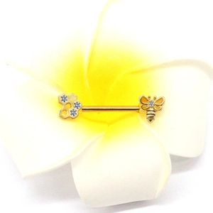 Détail d'un piercing de téton doré en acier avec nid d'abeille et abeille sur une fleur