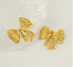 Détail de boucles d'oreilles nœuds dorés avec texture plissée et fermoirs à clous sécurisés