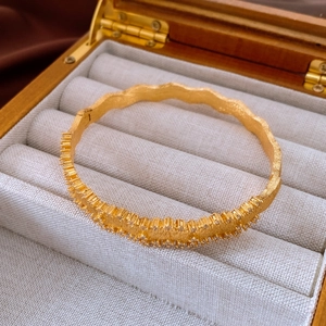 Detail of vintage gold-plated wave bangle with zircon stones and matte finish texture