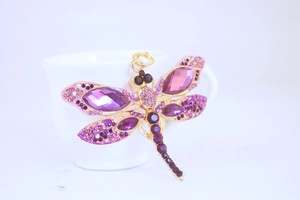 Macro shot of purple dragonfly pendant with crystals on a white ceramic surface