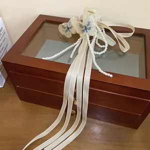Dettaglio dell'elegante molletta a farfalla con nastri crema e nappina di perle finte