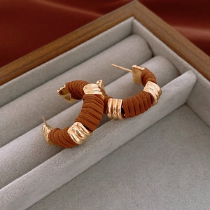 Macro view of C-shaped gold hoop earrings with brown textured wrap in jewelry box