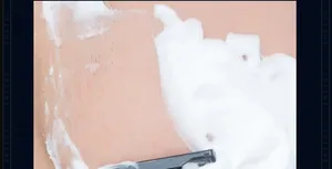 Macro shot of sandalwood shaving foam texture with a black razor blade on smooth skin