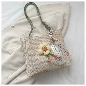 Detail of woven straw bucket bag with green straps and decorative floral silk scarf