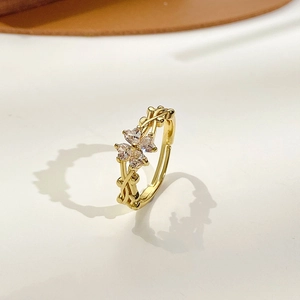 Elegant gold clover ring with heart-shaped crystals and vine band on a beige surface