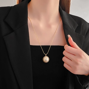 Close-up of champagne pearl pendant on a gold snake chain necklace worn by a model