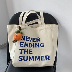 Detail of off-white canvas tote with blue text and orange fruit plush pendant