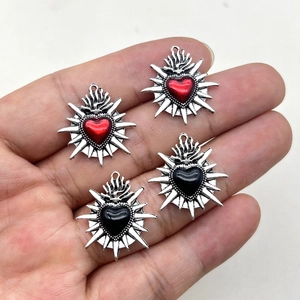 Vintage flaming sacred heart charms in red and black enamel held for size comparison