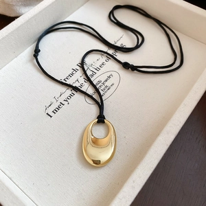 Gros plan d'un pendentif ovale doré sur un cordon noir posé sur un plateau texturé