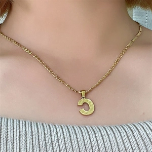 Dettaglio di una modella che indossa una collana dorata con ciondolo lettera C sul collo