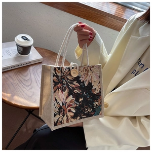 Detail of floral tapestry handbag featuring woven rope handles and a rustic wooden button