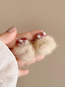 Close-up of red and white plaid heart earrings with soft beige pom-pom drops