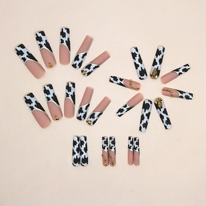 Cow print press-on nails set with gold accents and rhinestones on beige background