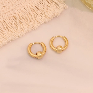 Detail of golden stainless steel hoop earrings with bead charms on marble surface