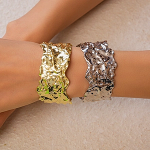 Detail of wide metal bangles with lava texture in gold and silver finish for women