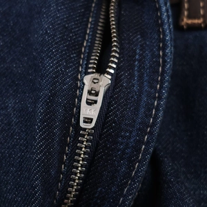 Gros plan d'une fermeture éclair YKK en métal argenté et coutures sur jean bleu foncé