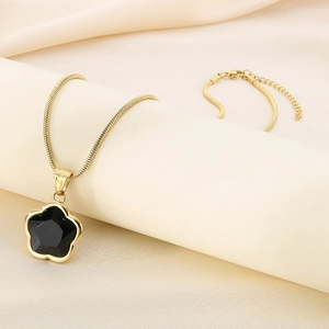 Detailed macro view of a black clover pendant on a gold snake chain over silk