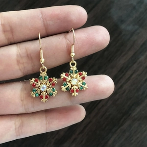 Detailed view of gold snowflake earrings with red and green rhinestones held in hand