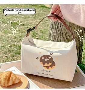 Detail of canvas lunch bag with adjustable brown handle and cute bagel print on grass