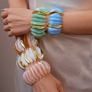 Close-up of colorful resin and gold metal bracelets layered on model's wrist