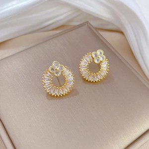 Macro shot of gold clover hoop earrings with micro-set white zircon on a silk display