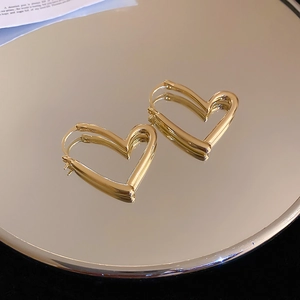 Detailed close-up of polished gold heart-shaped earrings on a reflective mirror surface
