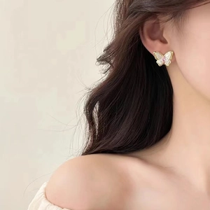 Close-up of small golden butterfly earrings with white pearl wings and pink crystals