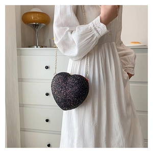 Detail of heart-shaped sequin crossbody bag with gold chain strap worn by a model