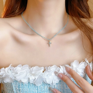 Close-up of a blue beaded choker with a gold-plated cross pendant on a woman's neck