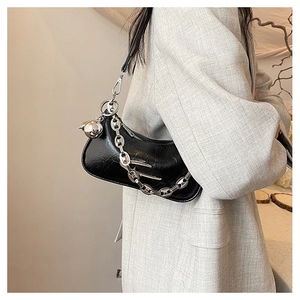 Close-up of black glossy leather crescent bag with bold silver chain and ball charm