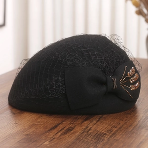 Detail of black wool beret with mesh veil and bead-decorated bow on wooden surface