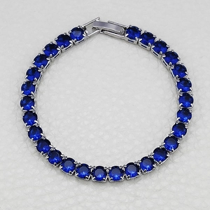 Detail view of silver tennis bracelet with round faceted dark blue sapphire stones