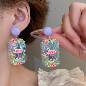 Close-up of acrylic flamingo earrings with tropical palm leaf and hibiscus floral print