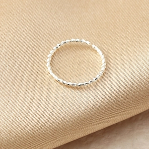 Dettaglio dell'anello da naso ritorto argento con trama su sfondo di tessuto beige