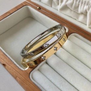 Detail view of gold and silver stainless steel bangles with zircon flower settings in a box