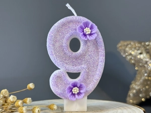 Close-up of purple glitter number 9 birthday candle with small decorative flowers