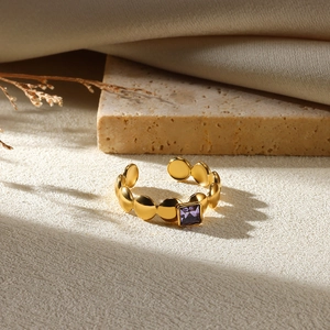 Detail of gold chain ring featuring a square purple gemstone set against a natural background
