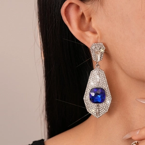 Macro detail of luxury geometric silver earrings featuring a large blue square gemstone