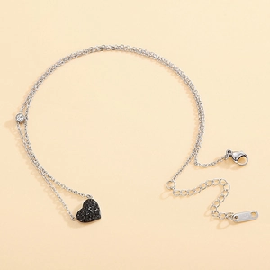 Détail d'une double chaîne argentée avec pendentif coeur noir et fermoir mousqueton