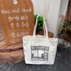 Outdoor view of a cream canvas tote bag featuring minimalist black bookstore illustrations