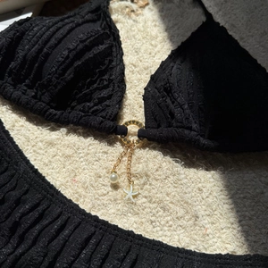 Detail of black textured bikini with pearl and starfish charms on a gold ring