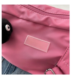 Détail du sac rose en tissu oxford avec un pendentif en peluche noir et une étiquette mode