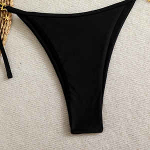 Detail shot of black high-cut bikini bottoms with a gold starfish charm on woven texture