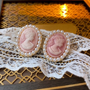 Close-up of vintage cameo earrings with pink portrait inlay and pearl border on lace