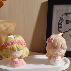 Detail of two cartoon girl candles with floral crowns on a white tray in a cozy home setting