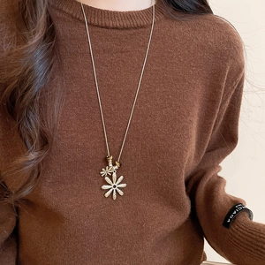 Detail of tiger eye bead and golden daisy flower pendants on long sweater chain