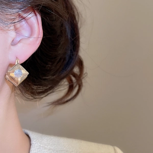 Detailed close-up of a model wearing a geometric diamond-cut rhombus ear clip in light gold