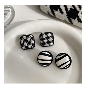 Detail of square houndstooth and round striped stud earrings on a white ceramic plate